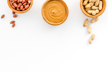 Peanut paste concept. Bowls with butter, nuts in shell, peeled nuts on white background top view copy space