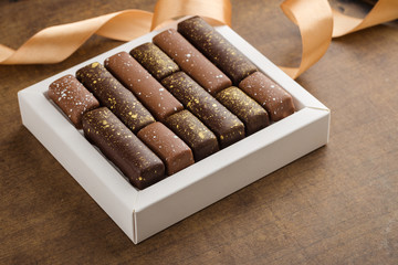 Handmade chocolate candies with golden splashes in box on wooden background