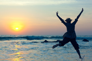 Young woman jumping with joy over the water at sunset
