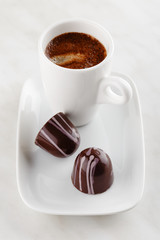 Handmade chocolate candy with purple splashes on plate with cup of coffee