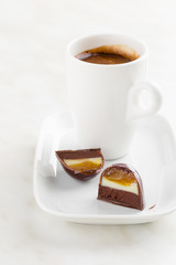 Cut handmade bonbon with ganache and fruit confiture filling with cup of coffee