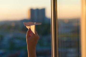 A girl is launching a paper airplane from a window at sunset. Support of the Telegram application...