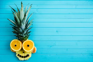 Muurstickers Funny applique from pieces of fruit on a turquoise wooden background. Fruit head made of pineapple, orange, copy space © wifesun