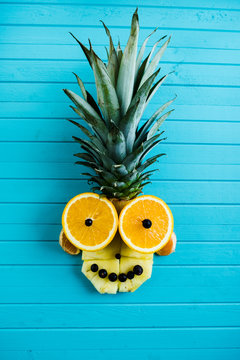 Funny applique from pieces of fruit on a turquoise wooden background. Fruit head made of pineapple, orange, vertical view.