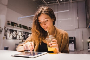 Obraz na płótnie Canvas Young business woman uses a tablet and drinks freshly squeezed orange juice from a straw in a cafe