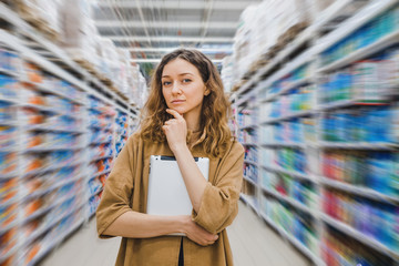 Young woman is thinking about shopping goods and about costs with a tablet in hand in supermarket