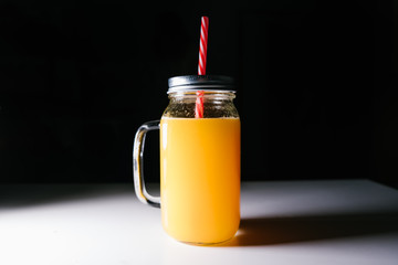 Orange juice in a glass jar with a handle on a black background