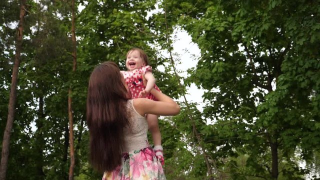 Mom throws baby high in air, laughing and playing with her in park. Mom and daughter laugh and rest in city.