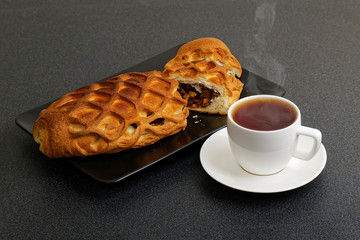 A cup of tea and homemade strudel with apples, raisin and cinnamon on dark table