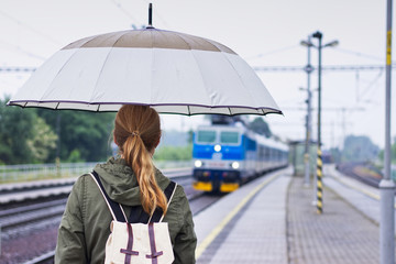 Backpacker woman with umbrella is traveling by train in rainy day