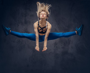 Fototapeta na wymiar Young blonde ballerina in sportswear dances and jumps in a studio. Isolated on a dark background.