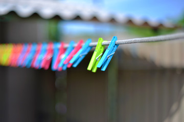 Fototapeta premium Color clothespins hang on the clothesline. laundry hook, colorful, pegs, rope ,outside, sun ,green, summer decorations, village, blue, sky , yellow ,red ,pins ,pink ,over