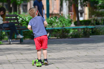 The boy skates on a scooter in the summer in the park, outdoor activities and outdoor sports for children.