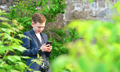 Naklejka na ściany i meble A boy with a camera is writing a message on a smartphone, on the street
