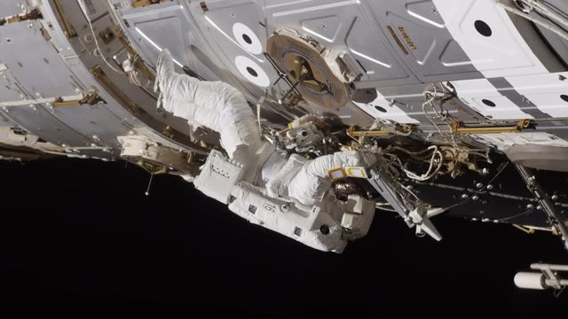 Astronaut works on outside of International Space Station, low angle