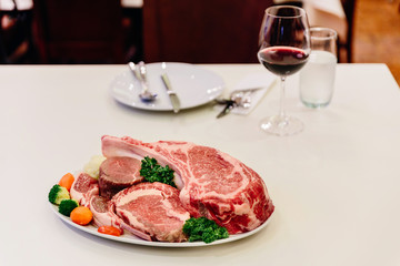 Different types of raw beef with fresh herbs and vegetables on the table for customer selection.