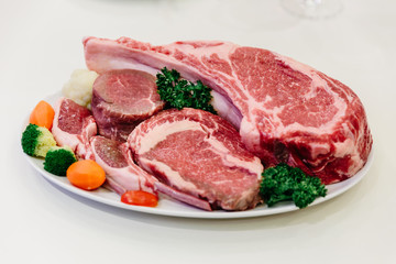 Different types of raw beef with fresh herbs and vegetables on the table for customer selection.