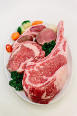 Different types of raw beef with fresh herbs and vegetables on the table for customer selection.