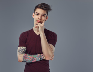 Handsome fashionable young guy with stylish hair and tattoo on his arm posing in a studio.