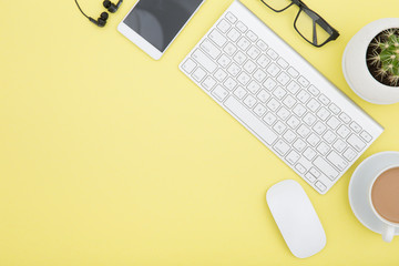 workspace with tablet, keyboard, coffee cup and eyeglasses copy space on yelow background. Top view.