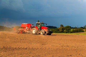 Obraz premium Red tractor in a dry field. Summer day at the farm in the Czech Republic. Agricultural work.