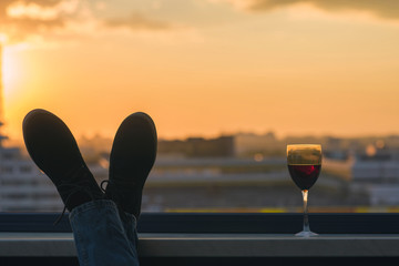 Silhouette of man feet with glass of red wine on the balcony on the city background