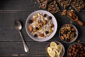 Breakfast with muesli in white bowl on gray natural desk with nuts and bananas around.