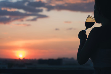Fototapeta premium Silhouette of woman hand with glass of red wine on sunset
