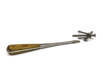 Old iron screwdriver with a wooden handle next to a bunch of different screws, isolated on a white background