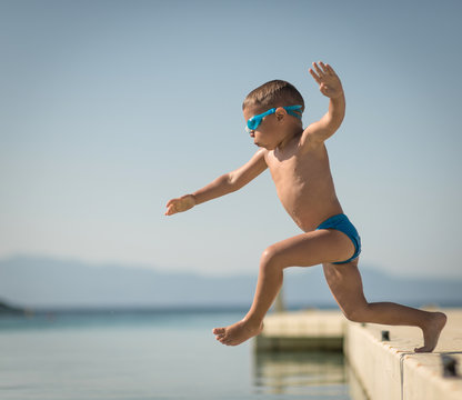 Little caucasian boy jumping in water from pier