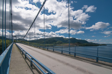 A picture of a bridge over the a channel over background with hills and clouds in a sunny day