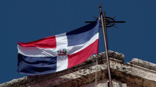 Flying national flag on the National Pantheon of the Dominican Republic with old cross 