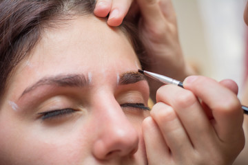 Beautiful young woman gets eyebrow correction procedure. Young woman painting her eyebrows in beauty saloon. close-up of a young woman plucking eyebrows with tweezers