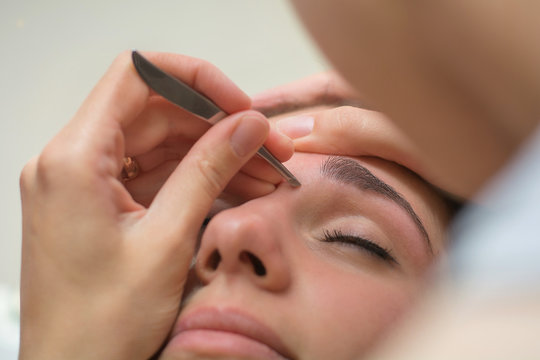 Beautiful Young Woman Gets Eyebrow Correction Procedure. Young Woman Painting Her Eyebrows In Beauty Saloon. Close-up Of A Young Woman Plucking Eyebrows With Tweezers