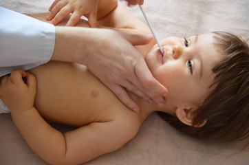 Male Pediatrician examining throat of a little ill girl. Kid looks sick and sad. Mother holding her kid. Doctor visit his patient with high fever at home. Doctor examining child with thermometer.