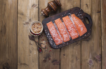 Fillet of salmon on the board, sea salt and spices. Preparation of a delicious and healthy dinner. Dietary food. Wooden background. place for text. Horizontal photo