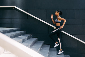 Side view of woman in sportswear  running up the steps in the city. Female athlete doing workout at...