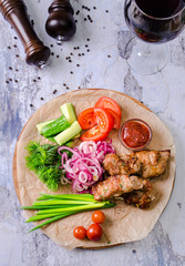Top view Kebabs - grilled meat and fresh vegetables on wooden board with red wine in a glass on background, restaurant menu concept. Beautiful juicy meat. Summer food outdoor.