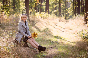 Naklejka na ściany i meble A young, blonde woman walking through the forest on a sunny autumn day.