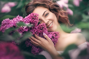 Close-up portrait of a young girl with long wavy hair in a spring garden with lilac flowers