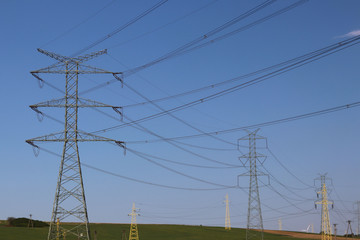 High voltage electric lines cross the hilly mestnost. Electric station in the summer under the open sky. Power industry. Ecology of nature. Metal technological structures. Strategic object at a field.