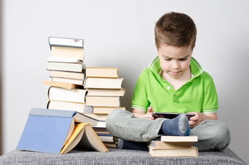 Kind sitzt auf der Sofa und spielt mit dem Smartphone neben Stapel Bücher