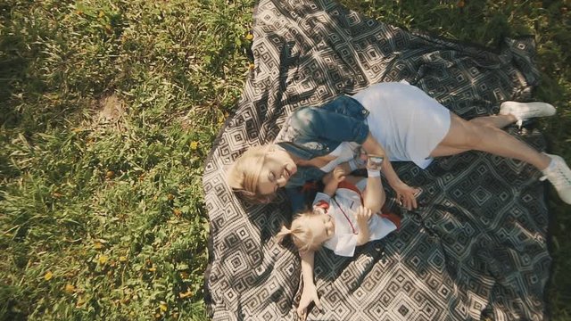 Family in city park outdoors. Mother and daughter lying on lawn. Happiness of motherhood and childhood in slow motion. Top view