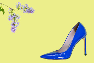 women's blue shoes as boat with a pointed nose on a high heel and a branch of the blossoming lilac on a yellow uniform background. the place for a text inscription. top view