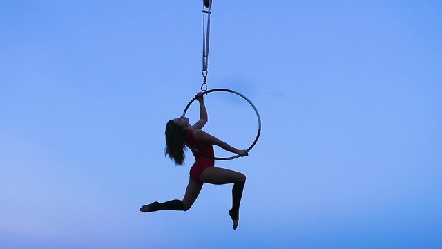 Silhouette of a woman performing tricks on a ring high in the sky.