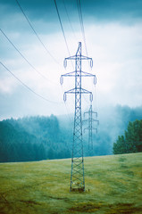 High voltage towers in a middle of forests and meadow. Electricity pylon with dark atmosphere in a...