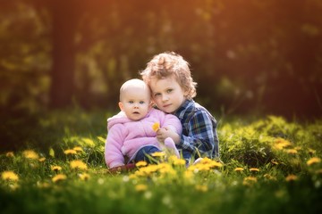 Naklejka na ściany i meble Beautiful caucasian children sitting and hugging on dandelion meadow