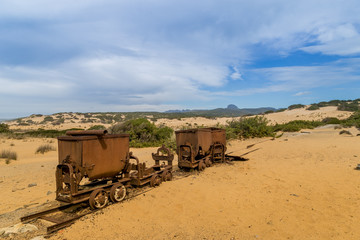 Old and rusty mine carts in the open air on the sand in Sardinia