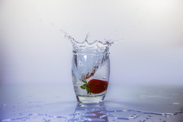 Bicchiere di acqua fresca con fragola tuffata dentro causando uno splash