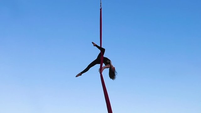 Woman performs sports tricks on ropes high in the sky.